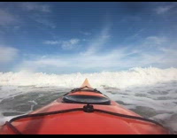 Orange kayak boat rides against ocean waves 
