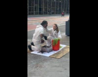 Man putting mud on body while woman wipes it off 