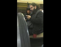 Man watches video on his phone with anime cartoon character mask next to him on subway train