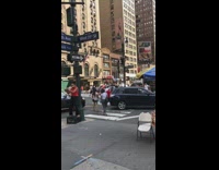 Man in orange tank top plays the flute stands on black crate on sidewalk