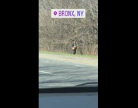 Guy walks alongside road while strumming guitar 