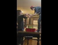 Guy standing on table at party feeds his friend noodles