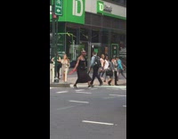 Man in tribal hat and red folding fan dances and crosses street while cars pass