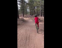 Dad rides behind son red shirt and falls on dirt trail