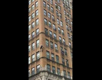 Two people scale brown building yellow stoplight 