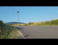 Guy goes fast downhill on longboard wearing shorts and red shirt