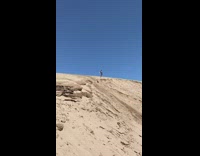 Guy jumps off sand dune and lands on his butt in the dirt at lake