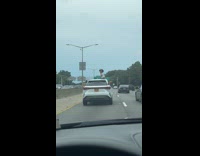 Woman on sunroof while dog peeks out window