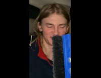 Two guys in car in backseat singing while holding blue broom