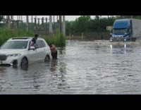 Shirtless man pushes white car from flooded road