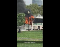 Leprechaun bus on fire in front of city skyline train tracks