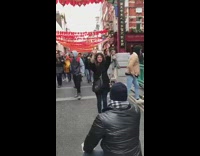 Woman holds up paper dancing dragon in front of Chinatown red lantern street