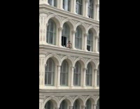 Man sitting on window ledge of apartment building