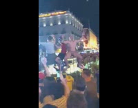 Naked man sits on fence in the middle of outdoor concert venue and parties