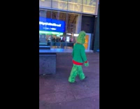 Grinch wearing green sweater walks around outside 