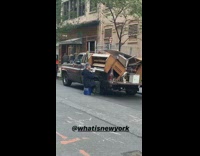 Man sits on blue Lowes bucket and plays wooden piano inside trunk of pick up truck on the street