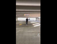Guy in black clothes in the middle of parking lot hits speed limit sign 