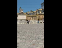 Two girls dance in front of palace statue