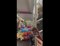 Guy selling large balloons with a lot of balloons on the subway train 
