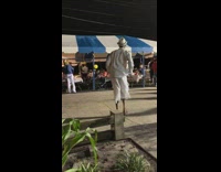 Guy in white shorts and hat dances at party next to blue white striped tent