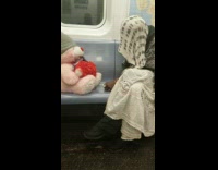 woman talks to pink bear next to her on train