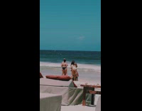 Woman in green bikini kneels with a drink at the beach