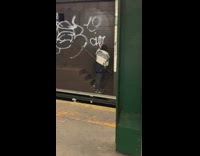 Guy graffiti tags a subway wall behind subway train tracks