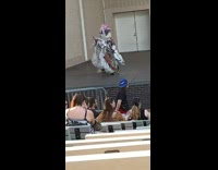 Performer in poofy dress and hat sings on amphitheater stage in front of crowd