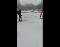 Guy and girl ski across park snow 