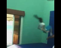 Girl frontflips off trampoline and face plants into blue safety mat on the wall