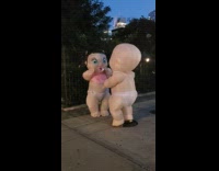 Giant two babies mascot walks along the street at night