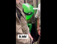 Person carrying inflatable alien on subway