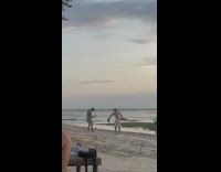 Man shirtless lifts two dumbbells on the beach