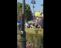 Woman pink shirt lays down and poses with hip in front of Disneyland castle