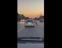 Man stick out the car window to film another car on the road