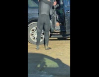 Guy takes black wetsuit off by car 