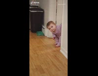 Purple onesie baby girl peeks out doorway 