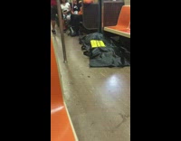 Person sleeps on subway train floor with black tarp sheet over their body