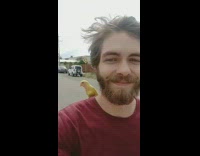 A man rides a bike with a yellow bird on shoulder