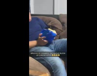 Guy takes bite out of block of cheese on couch