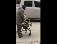 Old woman pushes a shirtless John Cena action figure around on her walker