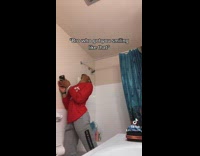 Guy in grey sweatpants red shirt in bathroom on phone 