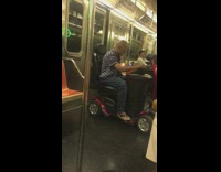 Old man on electric wheelchair bumps to music on phone on subway train