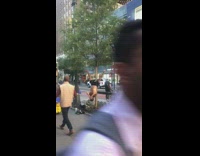 Man no shirt plays flutes hanging upside down tied to tree on sidewalk