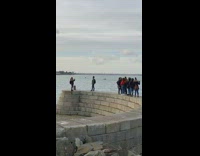 People stand on curved stone wall beach picture