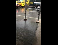 Pedestrian rides on sidewalk in the rain with black trash bag covering body and face