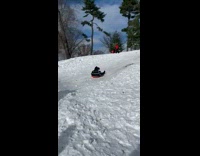 Girl rides orange sled down hill snow 