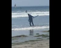 Guy in black wet suit walking slowly into water with flippers