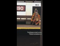 Man in orange blanket plays the flute in subway station
