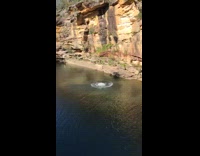 Black shorts guy jumps off cliff water 
